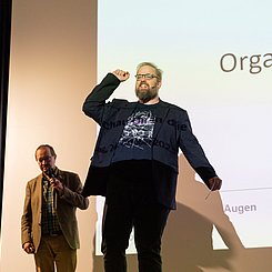 Sci-eeence Slam: Philipp Schrögel in Aktion. Links Till Pfeifer. Foto: Roxane Fijean/PHKA