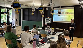 Zuhörende beim Vortrag von Heike Russ in einem Seminarraum sowie Heike Russ beim Vortragen, im Hintergrund sind ihre Folien zum Vortrag zu sehen